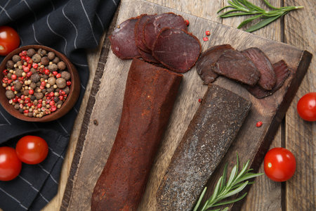 Delicious dry-cured beef basturma with rosemary and tomatoes on wooden table, flat layの写真素材