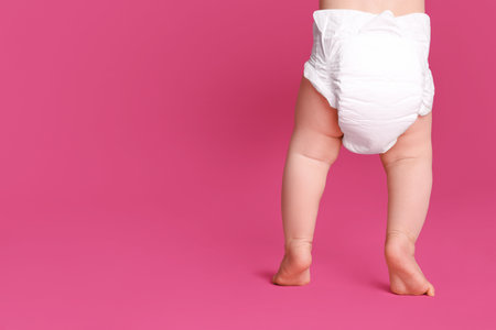 Back view of cute baby in dry soft diaper standing on pink background, closeup. Space for textの写真素材