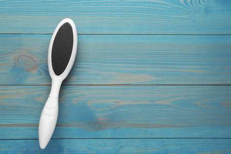 White foot file on light blue wooden table, top view with space for text. Pedicure tool