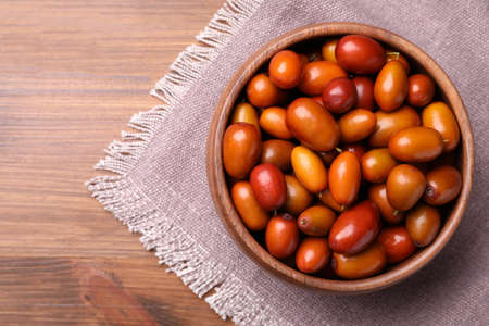 Fresh Ziziphus jujuba fruits in bowl with napkin on wooden table, top view. Space for textの写真素材
