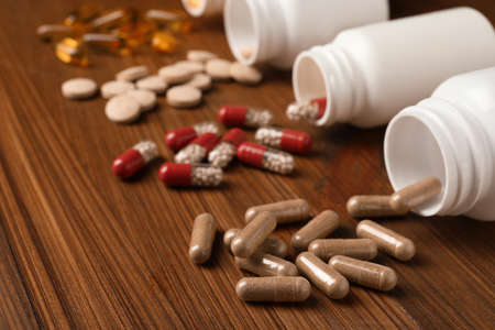Overturned bottles with different dietary supplements on wooden table, closeupの写真素材
