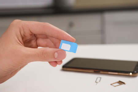 Woman with SIM card at white table indoors, closeup