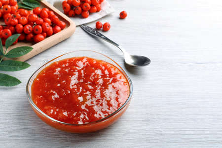 Delicious rowan jam in bowl on white wooden table. Space for text