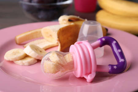 Nibbler with banana and fresh fruit on pink plate, closeup. Baby feederの写真素材