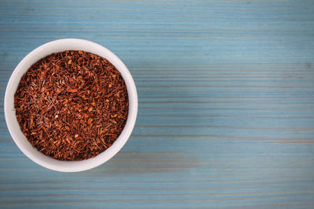 Dry rooibos leaves in bowl on turquoise wooden table, top view. Space for textの写真素材