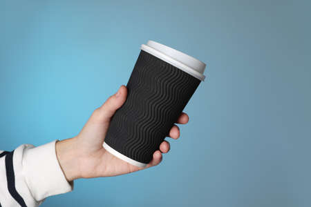 Woman holding takeaway paper coffee cup on blue background, closeup