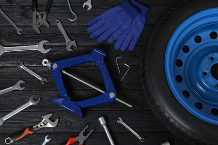 Car wheel, scissor jack, gloves and different tools on black wooden surface, flat layの写真素材