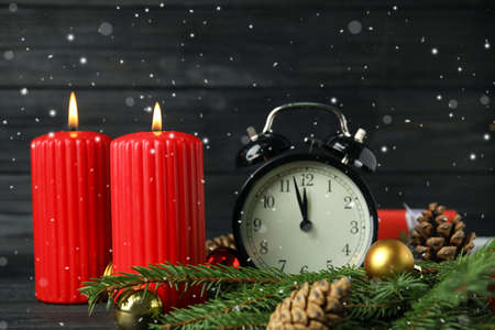 Snow falling on table with burning candles, alarm clock and festive decor. Christmas eve