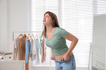 Young woman struggling to put on tight jeans at homeの写真素材