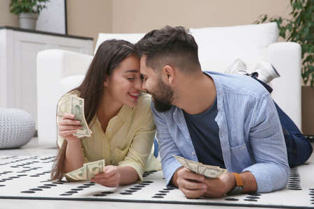 Happy couple with money on floor at homeの写真素材