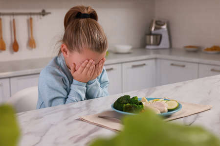 Cute little girl crying and refusing to eat dinner in kitchenの写真素材