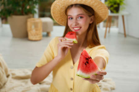 Beautiful teenage girl with slices of watermelon at home, focus on handの写真素材