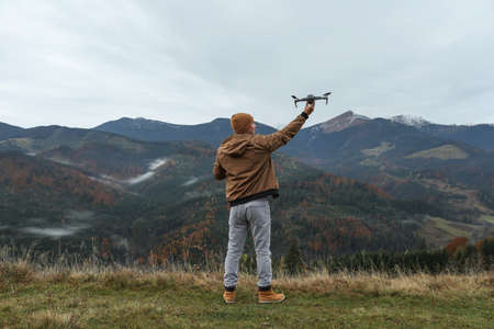 Young man with modern drone in mountains, back viewの写真素材