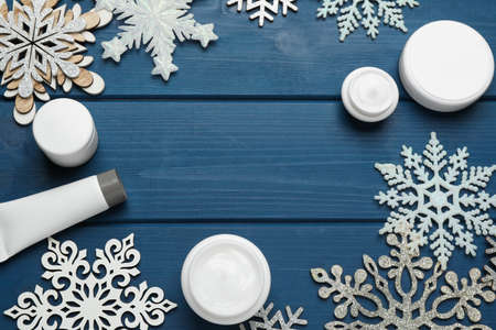 Frame of cosmetic products and snowflakes on blue wooden table, flat lay with space for text. Winter skin careの写真素材