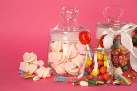 Glass jars with lots of different candies on bright pink backgroundの写真素材