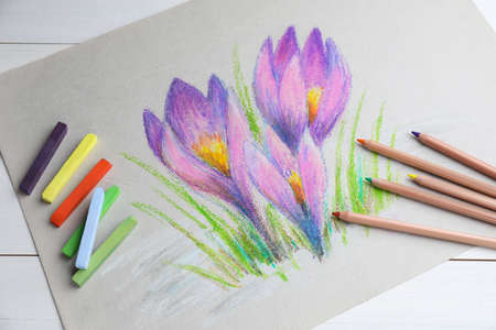 Colorful chalk pastels, pencils and beautiful painting of crocus flowers on white wooden table, above viewの写真素材