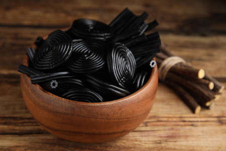 Tasty black candies and dried sticks of liquorice root on wooden table, closeupの写真素材