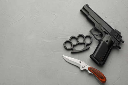 Black brass knuckles, gun and knife on light gray stone background, flat lay. Space for text
