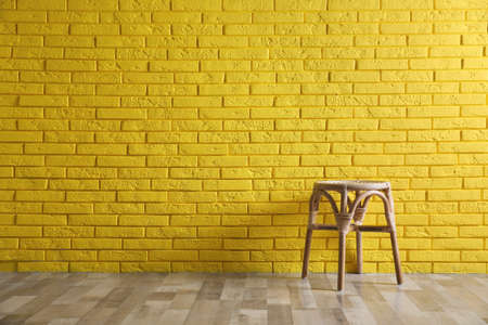 Stylish wooden stool near yellow brick wall, space for text. Interior elementの写真素材