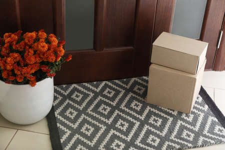 Cardboard boxes on stylish door mat and beautiful flowers near entranceの写真素材