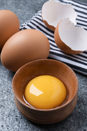 Raw chicken eggs and bowl with yolk on gray table, closeupの写真素材