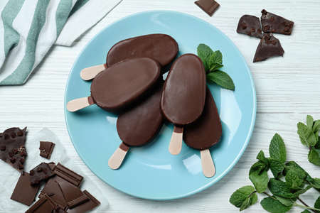 Flat lay composition with glazed ice cream bars, fresh mint and chocolate on white wooden tableの写真素材