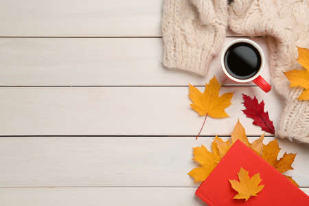Cup of hot coffee, book, sweater and autumn leaves on white wooden table, flat lay. Space for textの写真素材