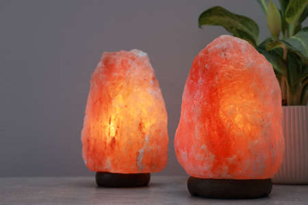 Himalayan salt lamps and houseplant on stone table near light gray wall