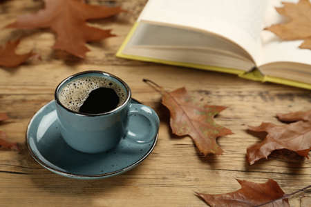 Cup of hot coffee, book and autumn leaves on wooden table, space for textの写真素材