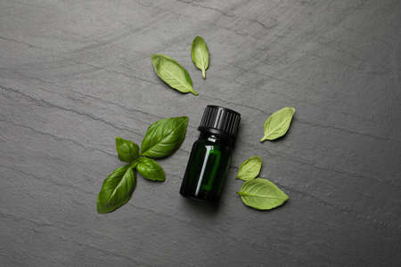 Bottle of essential basil oil and fresh leaves on dark gray table, flat layの写真素材