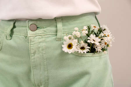Woman with beautiful tender flowers in pocket of jeans on light background, closeupの写真素材