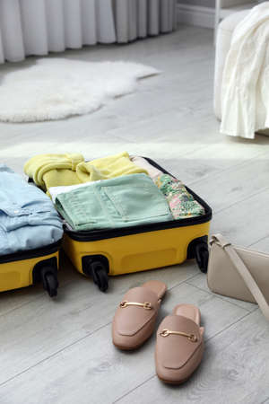 Open suitcase packed for trip, handbag and shoes on floor indoorsの写真素材