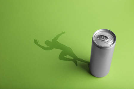 Energy drink and shadow in shape of sportsman's silhouette on light green backgroundの写真素材