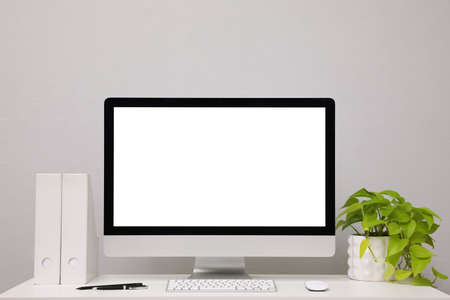 Comfortable workplace with blank computer display and plant on desk near light gray wall. Space for textの写真素材