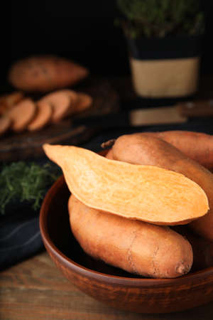 Cut and whole sweet potatoes in bowl on wooden tableの写真素材
