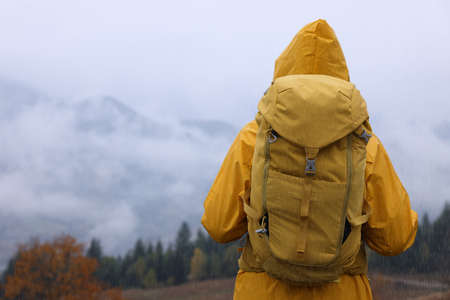 Woman in raincoat with backpack enjoying mountain landscape during rain, back viewの写真素材