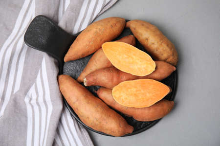 Slate board with cut and whole sweet potatoes on light gray table, top view