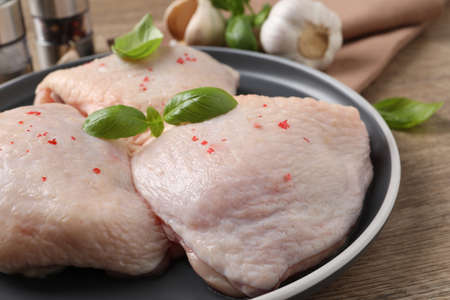 Raw chicken thighs with basil on wooden table, closeupの写真素材