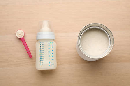 Feeding bottle with infant formula and powder on wooden table, flat layの写真素材