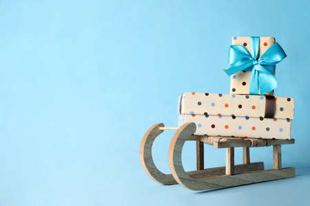 Wooden sleigh with Christmas gift boxes on light blue background, space for textの写真素材