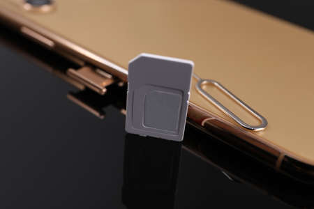 SIM card, smartphone and ejector on black background, closeup