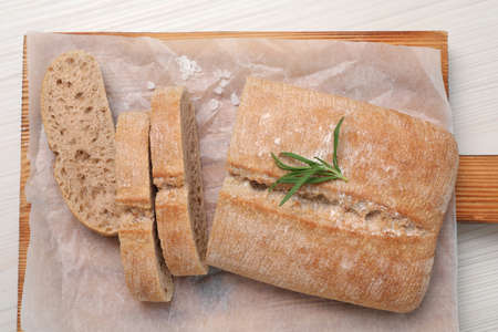 Fresh crispy ciabatta with rosemary on white wooden table, top view