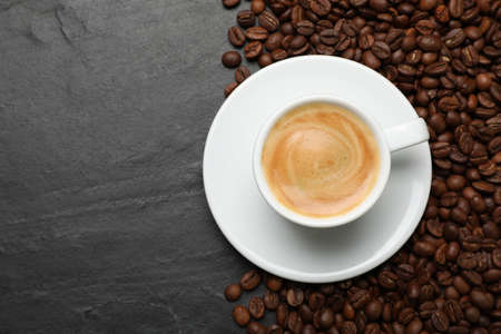 Cup of hot drink and beans on black table, top view with space for text. Coffee break