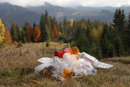 Pile of plastic garbage on grass against mountain landscapeの写真素材