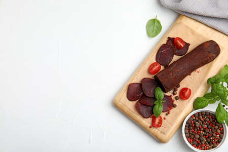 Delicious dry-cured beef basturma with basil, peppercorns and tomatoes on white table, flat lay. Space for textの写真素材