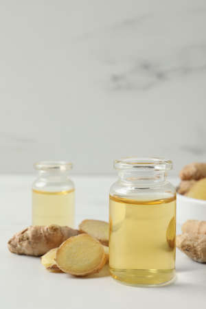 Glass bottle of essential oil and ginger root on white tableの写真素材