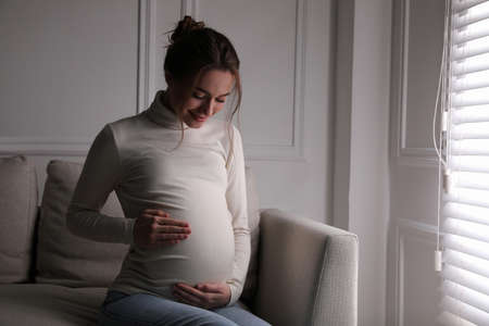 Young pregnant woman sitting on sofa at homeの写真素材