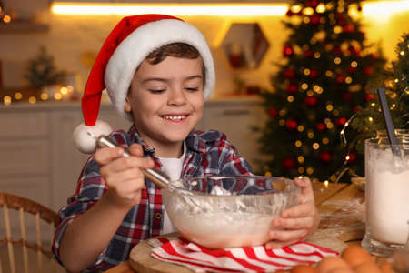 Cute little boy in Santa hat making dough for Christmas cookies at homeの写真素材