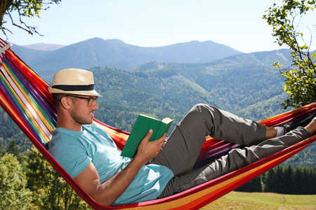 Handsome man reading book in hammock outdoors on sunny dayの写真素材