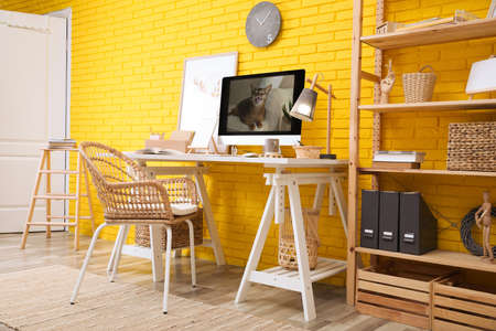Stylish home office interior with comfortable workplace near yellow brick wallの写真素材